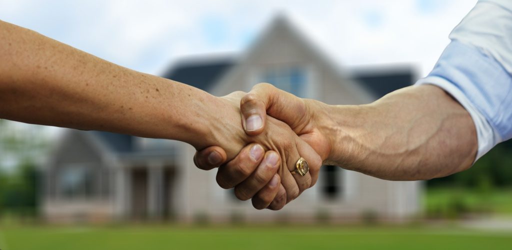 Two people shaking hands in front of house
